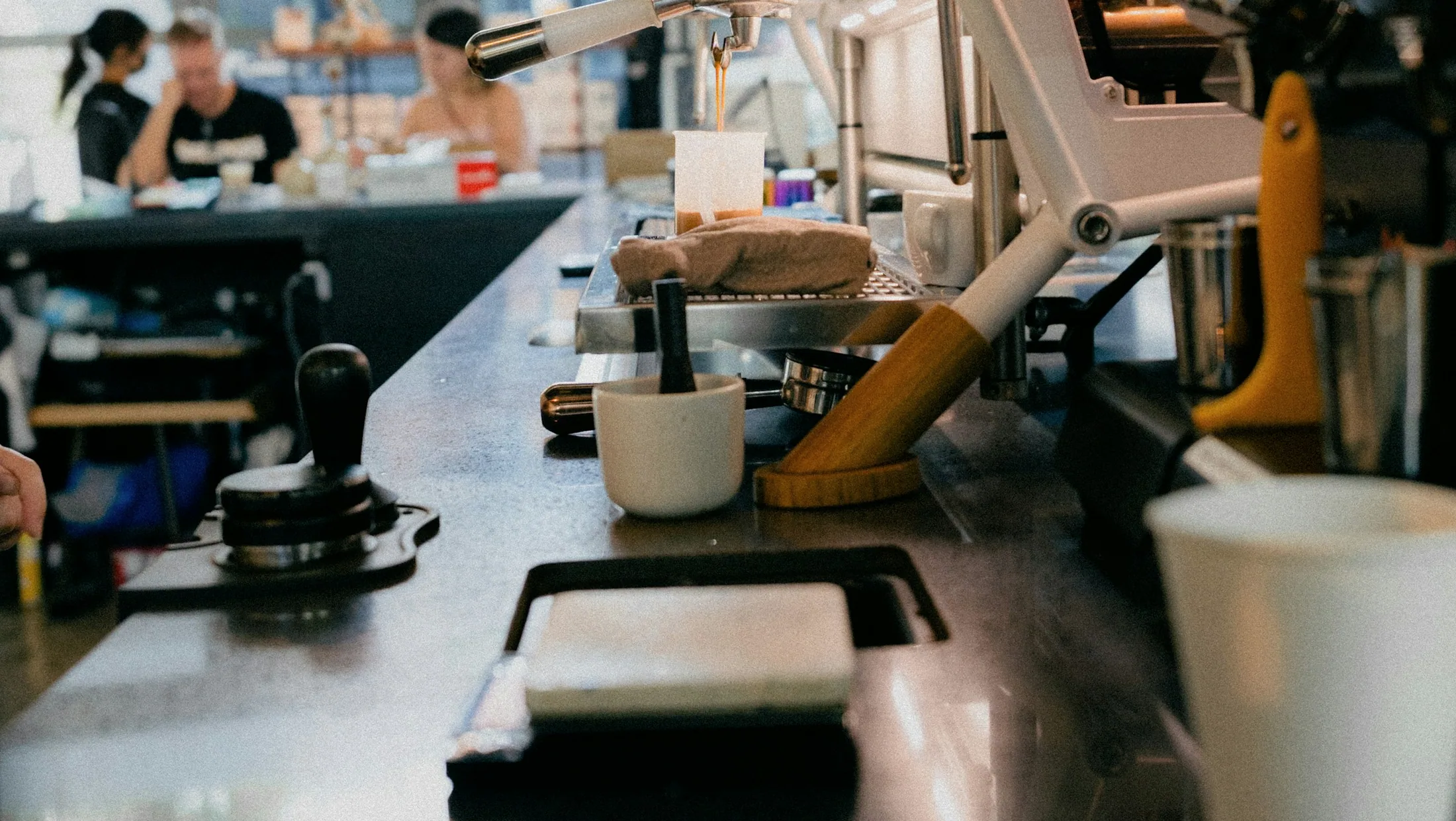 A real Singapore cafe counter with an espresso machine and customers in soft focus.